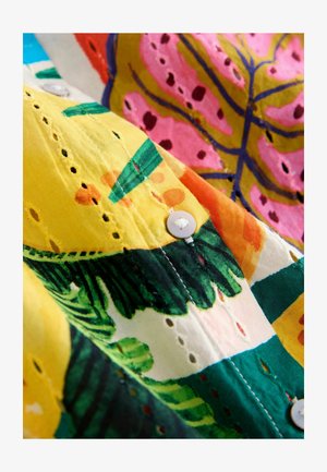 Šarena tkanina s uzorcima listova u žutoj, zelenoj, ružičastoj i narančastoj boji. Uz rub su vidljivi bijeli gumbi i izrezani otvori u obliku oka.