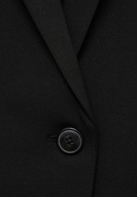 Gros plan d'une veste noire sur mesure avec un revers cranté et un seul bouton noir quatre trous fermé.