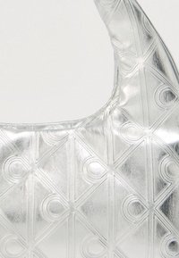 Ασημένια μεταλλική τσάντα χειρός με ραμμένο σχέδιο σε σχήμα διαμαντιού. Στρογγυλεμένο σχήμα και ομαλή υφή, με ανάγλυφες κυκλικές λεπτομέρειες.