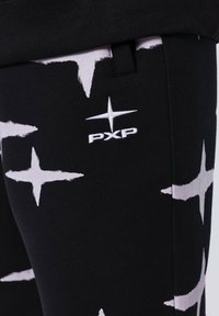 Pantalones negros con un gran patrón de estrellas blancas, hechos de una tela suave, con un logotipo bordado "PXP" en el lateral.