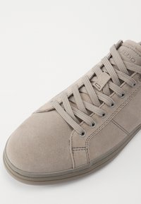 Tenisii înalți din suede gri, cu șireturi gri și vârf întărit, având detalii de cusătură discrete și o talpă din cauciuc.