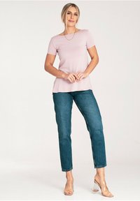 Jasnoróżowa koszulka z krótkim rękawem i okrągłym dekoltem, zestawiona z niebieskimi dżinsami o prostym kroju i przezroczystymi sandałami na obcasie. Prosty design i miękka tekstura.