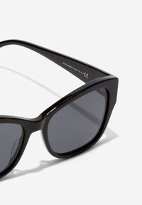 Gafas de sol de gran tamaño y forma de ojo de gato en color negro, con montura suave, lentes oscuros y un diseño angular audaz. Presentan un acabado brillante y una marca mínima.
