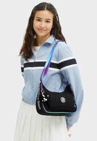 Borsa a spalla in tessuto nero con tracolla multicolore, dotata di una tasca frontale e dell'iscrizione "Dare to Dance". Include un piccolo ciondolo decorativo.