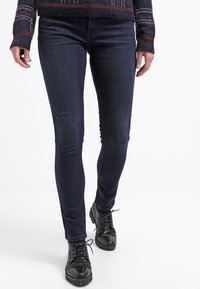 Smala jeans i mörk denim, med en klassisk passform. Bärs med svarta texturerade snörskor. Outfiten fulländas av en mönstrad tröja.