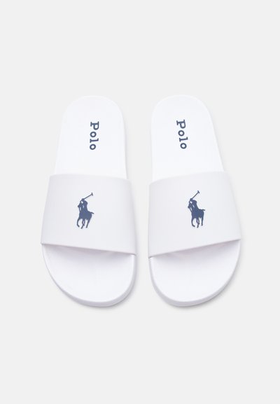 Ζευγάρι λευκών σαγιονάρων της μάρκας Polo με λογότυπα παίκτη πόλο σε ναυτικό μπλε σε φαρδιές λουράκια και το κείμενο "Polo" στις σόλες.