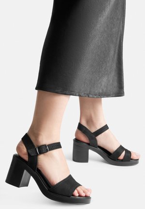 Sandale negre cu toc, cu finisaj texturat, mat. Prezintă un design cu vârful deschis, curea ajustabilă la gleznă și un toc gros.