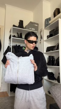 Felpa grigia con zip tenuta da una persona, caratterizzata da un tessuto morbido e strutturato. La felpa è piegata con dettaglio della zip visibile, mostrando un design casual.
