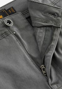 Graue Jeans mit einem stabilen Reißverschluss, sichtbaren Nähten und einem Knopf. Sie verfügen über einen strukturierten Innenbund und ein Stoffetikett.