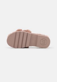 Semelle d'un chausson en fausse fourrure rose avec des stries texturées et le logo MK embouti près du talon sur un fond blanc uni.