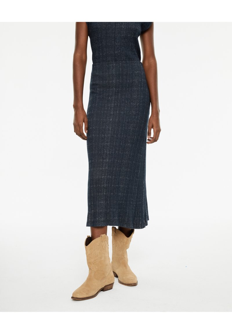 Vestido de punto en azul oscuro con una textura acanalada, complementado con botas de vaquero de ante marrón claro que presentan un bordado decorativo y un tacón bajo.