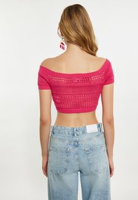 Fukszia, vállnélküli, kötött crop top, textúrált dizájnnal. Világoskék, magas derekú farmernadrággal párosítva, hátsó zsebekkel.