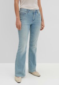 Light blue flared jeans made of denim, featuring a five-pocket design, subtle fading, and worn edges at the hems. Paired with light footwear.