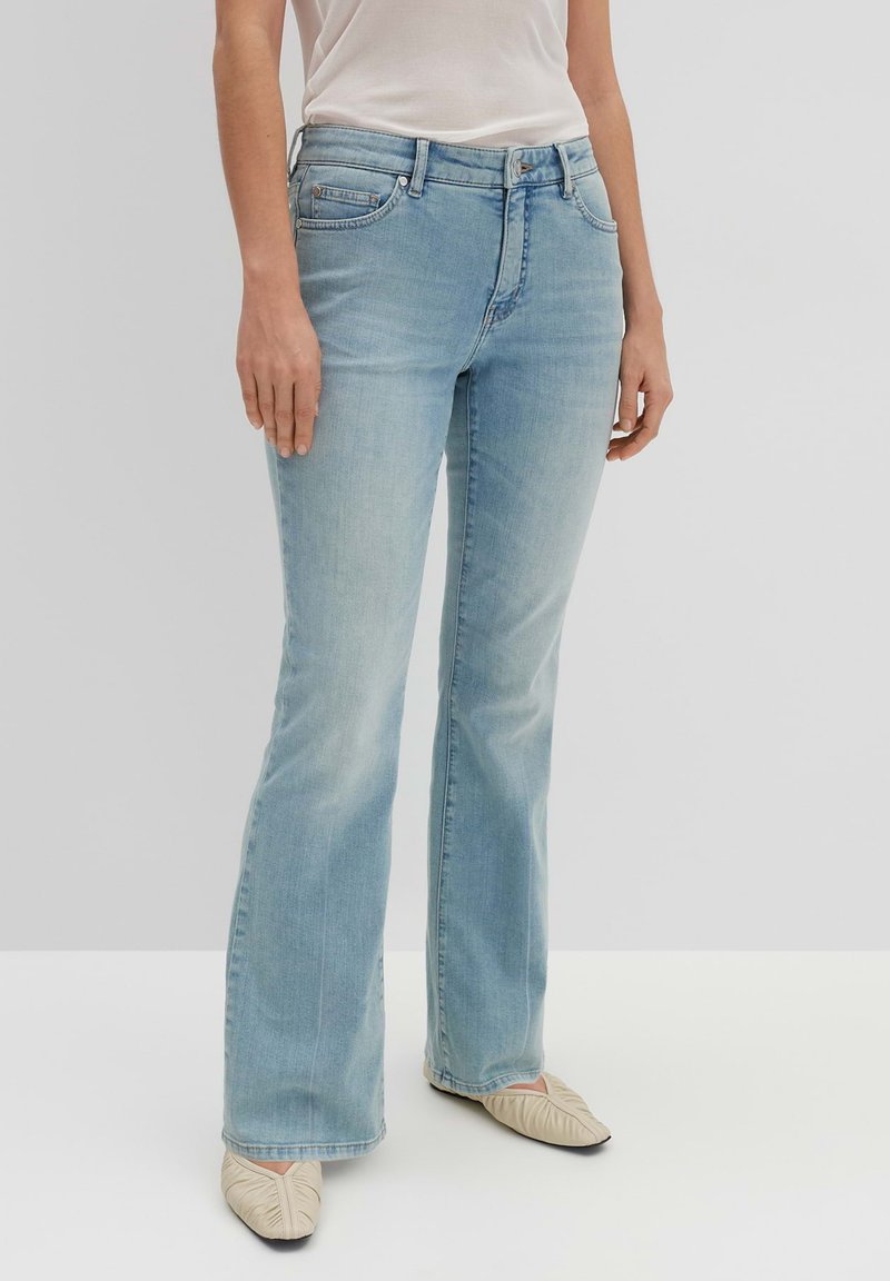 Light blue flared jeans made of denim, featuring a five-pocket design, subtle fading, and worn edges at the hems. Paired with light footwear.