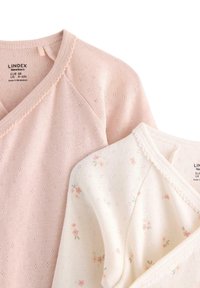 Twee pasgeboren shirts met lange mouwen: de ene roze met gestructureerde stippen, de andere wit met kleine bloemmotieven. Beide hebben een V-hals en een delicate afwerking.