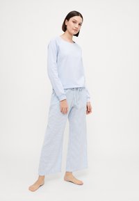 Ljusblå sweatshirt med långa ärmar tillsammans med randiga pyjamasbyxor. Byxorna har en lös passform och dragsko i midjan. Slät tygtextur.