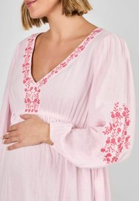 Rochie roz din in cu decolteu în V, decorată cu broderie florală de un roz mai închis pe decolteu și mâneci, și cu elastic strâns la talie.