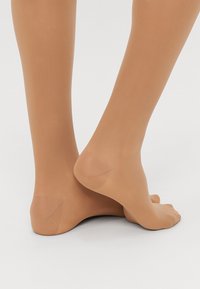 Collants beige transparents avec une texture lisse, dessinés pour s'adapter aux pieds et aux jambes, présentant un renfort au niveau des orteils et des chevilles conçu pour le confort.