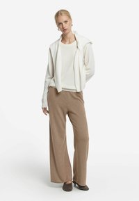 Lättvit tröja i lager med tan färgade stickade byxor. Tröjan har huva och långa ärmar. Vida ben byxor gjorda av mjukt material.