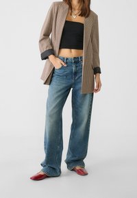 Blazer de cuadros marrón con puños negros, top corto negro, vaqueros anchos de color azul claro y zapatos rojos de tipo slip-on. Enfocado en el layering y un ajuste casual.