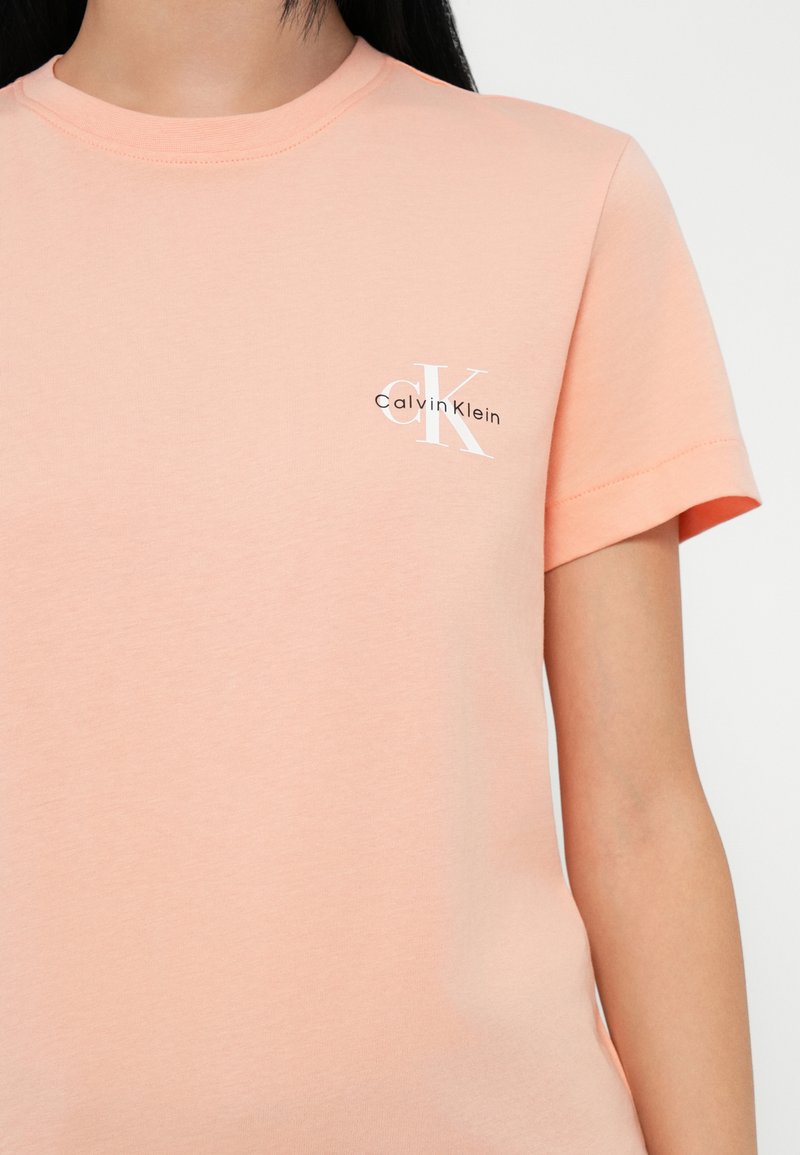 Camiseta de algodón rosa claro con cuello redondo y mangas cortas, con un pequeño logo blanco de Calvin Klein en el lado izquierdo del pecho.