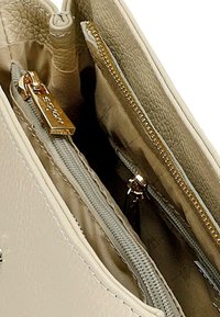 Interno di una borsa a mano in pelle beige con molteplici tasche, zip dorate e foderatura testurizzata. Una tasca ha un'etichetta con la lettera "S" impressa.