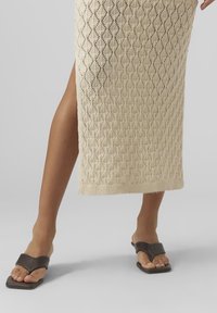 Knit midi skirt in light beige with diamond pattern, side slit and ribbed hem. Paired with dark brown flat sandals with a square toe.