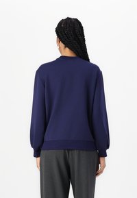 Tmavě modrá mikina s kulatým výstřihem, dlouhými balónovými rukávy a ribbovaným lemem. Měkká látka, minimalistický design a volný střih.