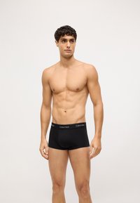 Crne pamučne bokserice s prilagođenim krojem i elastičnom pojasom na kojem se nalazi logo Calvin Klein. Model stoji uspravno nasuprot neutralnoj pozadini.