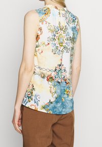 Haut sans manches à imprimé floral aux couleurs pastel, avec des motifs délicats en bleu, jaune et vert. Tissu doux avec un col froncé.