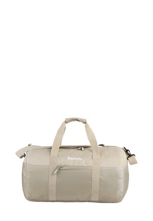 Sac de voyage beige en tissu durable, avec un panneau avant texturé, des poignées doubles et une bandoulière réglable.
