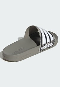 Le ciabatte Adidas presentano una suola in gomma grigia, una fascia a strisce bianche e nere con il marchio e un plantare texturizzato per una migliore aderenza.