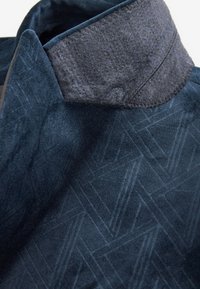 Col de veste bleu marine avec doublure en polaire douce gris foncé et motif géométrique subtil sur le tissu extérieur.
