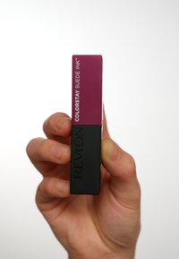 Produkt do ust Revlon Colorstay Suede Ink w prostokątnym opakowaniu; górna część jest ciemnofioletowa z etykietą, a dolna jest matowa czarna z wytłoczonym logo.
