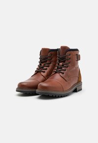 Botas de tobillo de cuero marrón con diseño de cordones, cuello acolchado y acentos de ante color marrón claro. Cuenta con una suela de goma texturizada para mayor agarre.