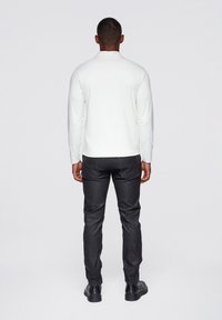 Weißes langärmliges Hemd, figurbetontes Design, kombiniert mit schwarzen, schmal geschnittenen Hosen, glatte Textur und schwarzen Schuhen. Rückansicht.