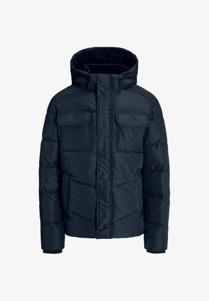 Tumesinise puffjakiga, millel on kapuuts, nelja esist taskut ja quiltitud disain, kantud valge T-särgi ja mustade pükste kohal, koos tennisetossudega.