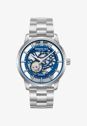 Orologio automatico in acciaio inossidabile argentato con quadrante scheletrato blu. Presenta indicatori delle ore prominenti, ingranaggi a vista e un bracciale a maglie metalliche.
