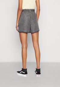 Shorts en denim gris taille haute avec une ceinture, ourlets roulés et une coupe décontractée, associés à des baskets montantes noires.