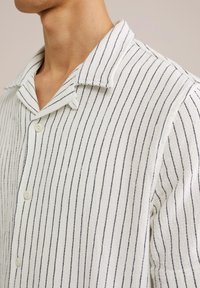 White button-up shirt with navy vertical stripes, made of textured fabric. Features a short collar and visible button closure.