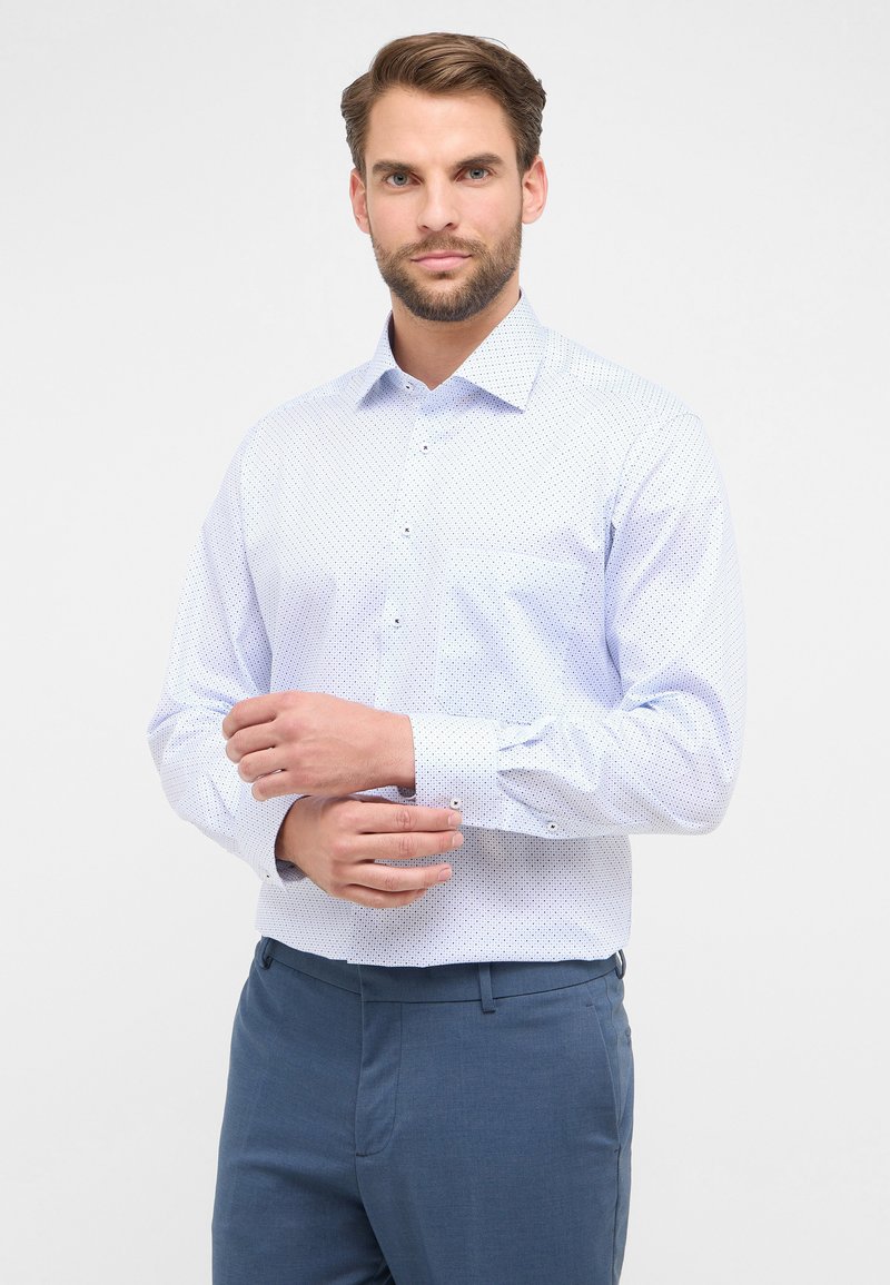 Camicia button-up di un blu chiaro con un motivo a pois. Maniche lunghe e colletto a punta. Il tessuto sembra liscio e leggero.
