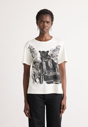 Woman wearing white t-shirt with black panther in scarf leaning from car window, paired with black pants with subtle dots.