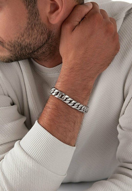 Bracciale in argento al polso, caratterizzato da catene spesse e intrecciate con una superficie lucida. La luce si riflette sulla texture liscia.