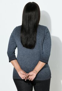 Szary, teksturowany top z rękawami o długości do łokcia i zaokrąglonym dołem, w połączeniu z ciemnymi dżinsami. Włosy opadają prosto na plecy.