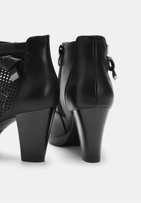 Black high-heeled ankle boots with a smooth leather finish, textured cut-out design, and a side zipper. Features a sturdy block heel.