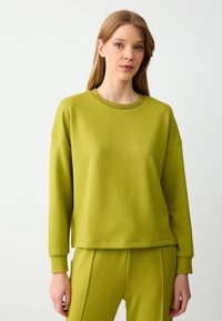 Sweatshirt vert lime en tissu doux avec un col rond, un col à côtes et une coupe décontractée. Associé à un pantalon de jogging assorti.