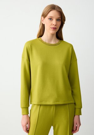 Felpa verde lime in tessuto morbido con scollo rotondo, colletto a coste e vestibilità rilassata. Abbinata a pantaloni della tuta coordinati.