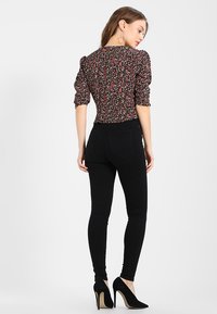 Blusa nera a fiori con maniche a sbuffo, caratterizzata da un design aderente. Abbinata a jeans skinny neri a vita alta e tacchi a stiletto.