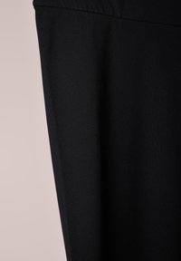 Zwarte stof met een gladde textuur, aansluitend ontwerp en minimalistische stijl. Naaddetail langs de bovenrand. Geen zichtbare patronen of accenten.