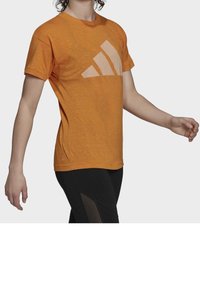 Krátký rukáv oranžové tričko s velkým světle oranžovým logem Adidas, vyrobené z texturované tkaniny s uvolněným střihem.